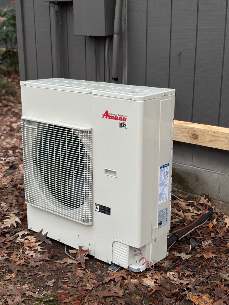 Amana R32 outdoor heating and air conditioning unit installed beside a house exterior