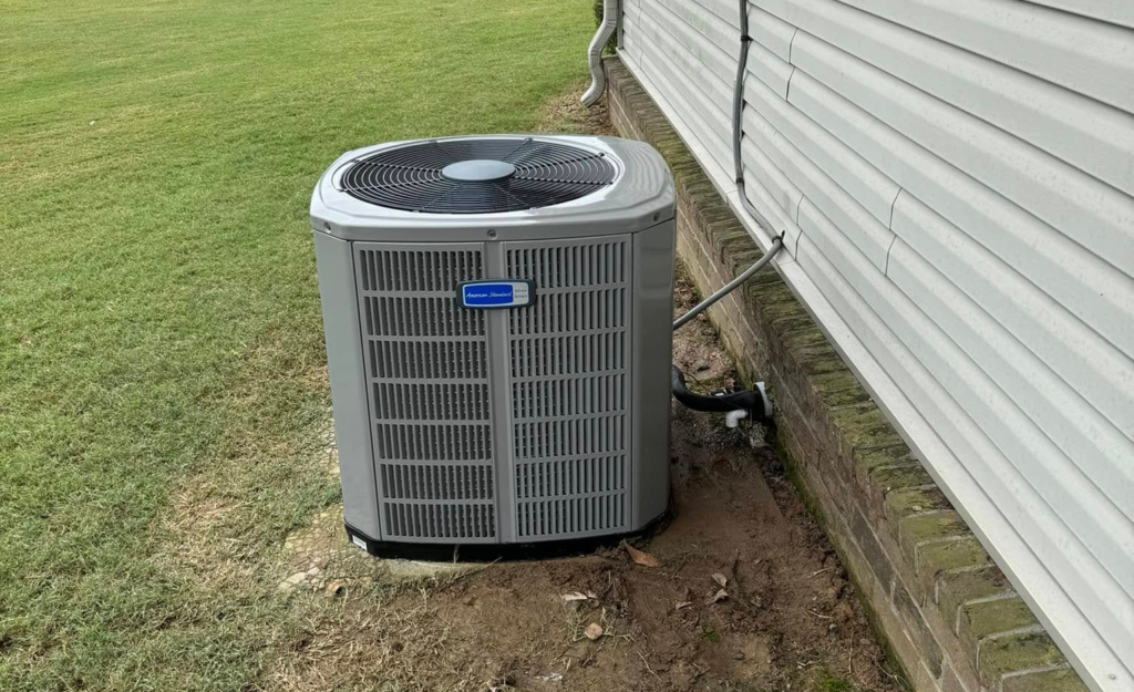 American Standard outdoor AC condenser unit installed beside a house with white siding and a grassy yard