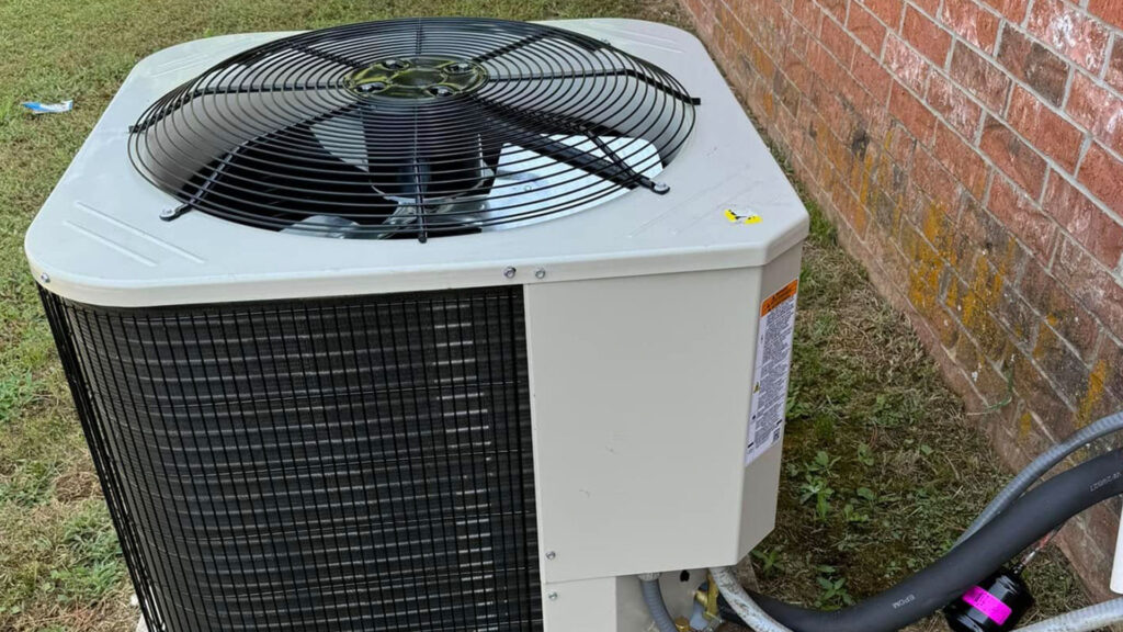 Outdoor air conditioning condenser unit installed beside a brick wall with refrigerant lines connected at the base