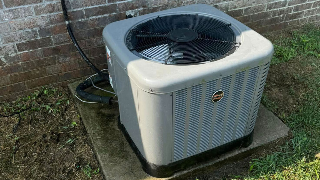 Ruud outdoor air conditioning condenser unit installed on a concrete pad against a brick wall